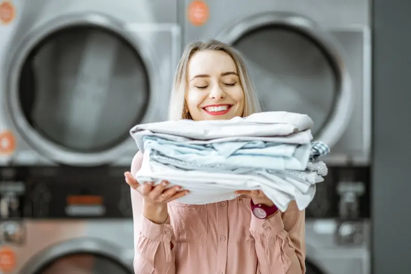 Vrouw houdt een stapel opgevouwen was vast voor wasmachines